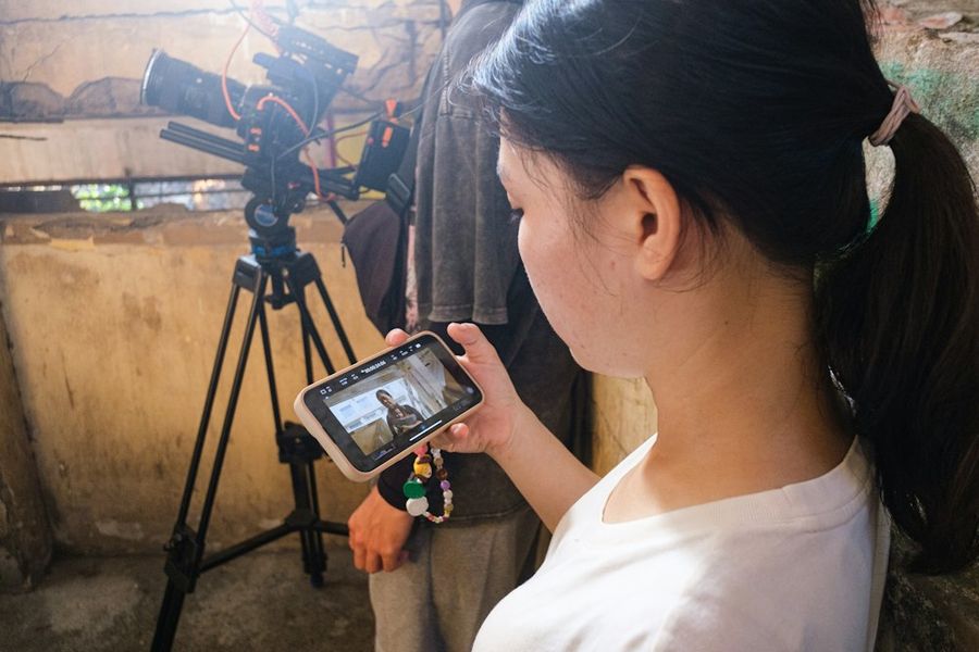 Cô gái xem lại cảnh quay trên điện thoại cạnh chân máy